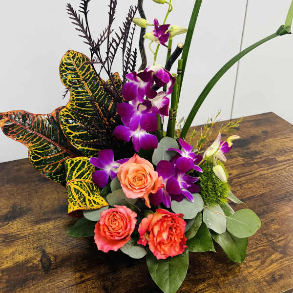 Tropical floral arrangement with purple orchids and coral roses