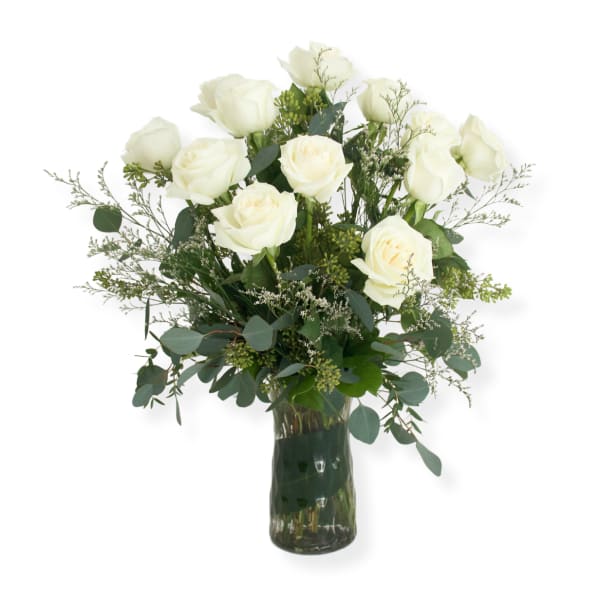 White roses arranged in a clear glass vase with airy greenery