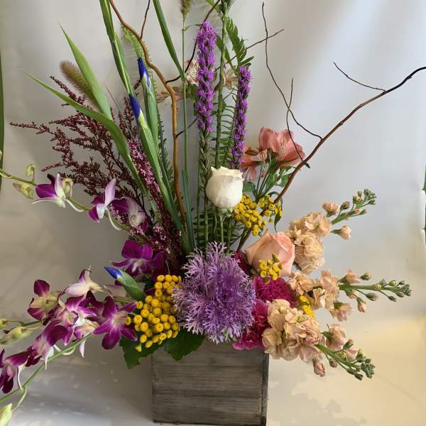 Tall mixed floral arrangement in a wooden box with purple orchids and peach blooms