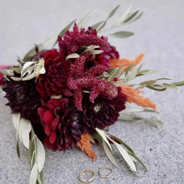 Deep red bouquet with orange accents and two rings on a stone surface