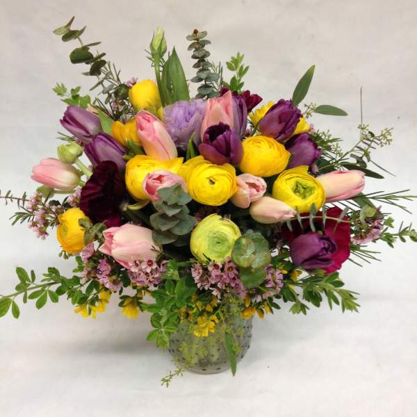 Colorful arrangement of yellow ranunculus and pink and purple tulips in a clear glass vase.