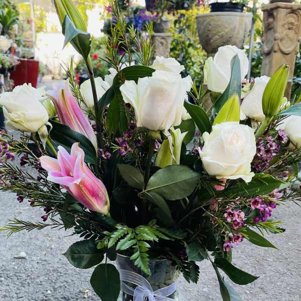 White roses and pink lilies arranged in a glass vase with a ribbon.