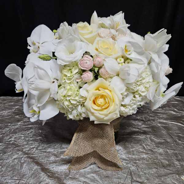 White floral bouquet with roses, orchids, and hydrangeas tied with burlap ribbon