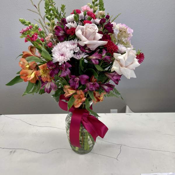 Mixed pink, white, and orange flowers arranged in a glass vase with a ribbon.