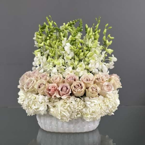 White and blush roses with white orchids in a white ceramic vase