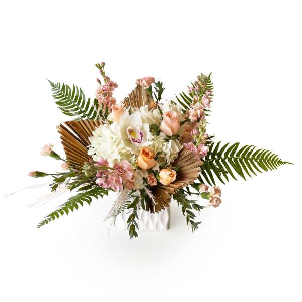Peach and white floral arrangement in a white vase with palm fronds