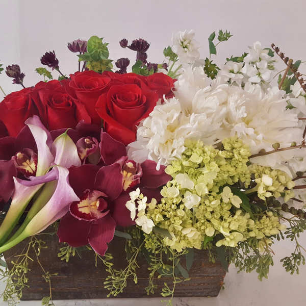 Mixed floral arrangement with red roses, white blooms, and burgundy orchids in a wooden box