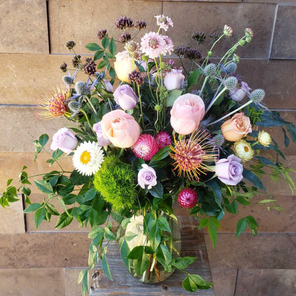 Mixed bouquet of pastel roses and assorted blooms in a glass vase