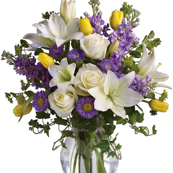 Bouquet of white lilies, roses, purple flowers, and yellow tulips in a glass vase