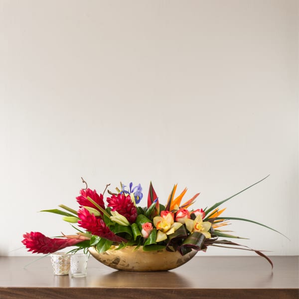 Tropical flower arrangement in a gold bowl with red, orange, and yellow blooms