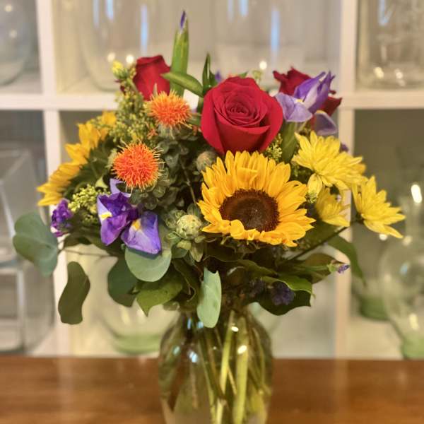 Mixed bouquet of sunflowers, red roses, and purple flowers in a glass vase