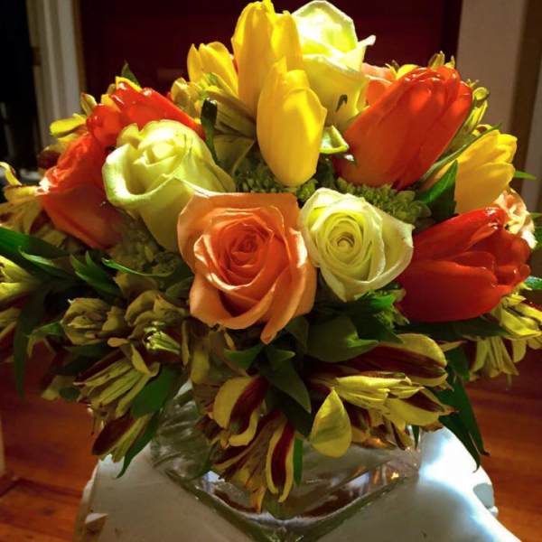 Bouquet of orange, yellow, and white roses in a clear glass vase