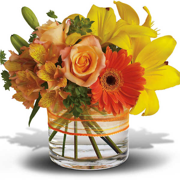 Bouquet of yellow lilies, orange roses, and a gerbera daisy in a glass vase