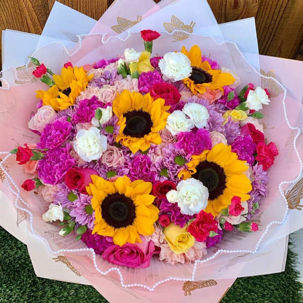 Bouquet of sunflowers, roses, and carnations wrapped in pink paper
