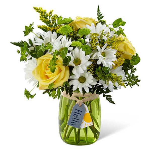 Yellow roses and white daisies with green accents in a green glass jar with a hello tag