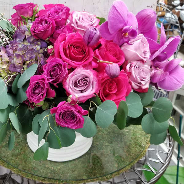 Pink and purple rose arrangement with orchids in a white vase