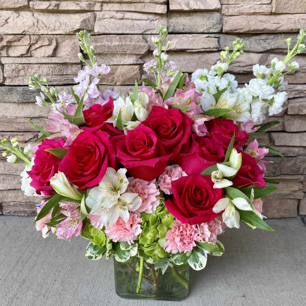 Bouquet of red roses, pink carnations, and white alstroemeria in a glass vase