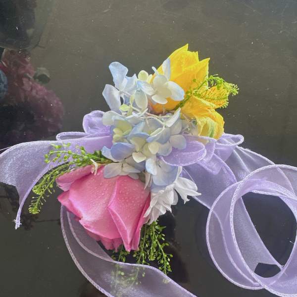 Small bouquet with pink and yellow roses and pale blue flowers tied with lavender ribbon