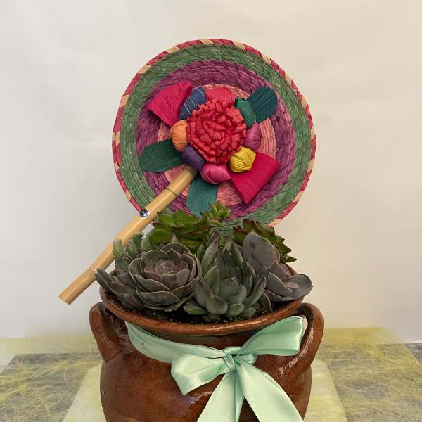 Succulent arrangement in a brown pot with a colorful woven fan and mint ribbon