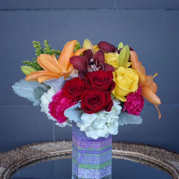Mixed bouquet of roses, lilies, orchids, and carnations in a glass vase