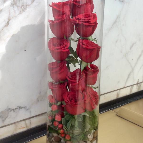 Tall glass cylinder with red roses and pebbles