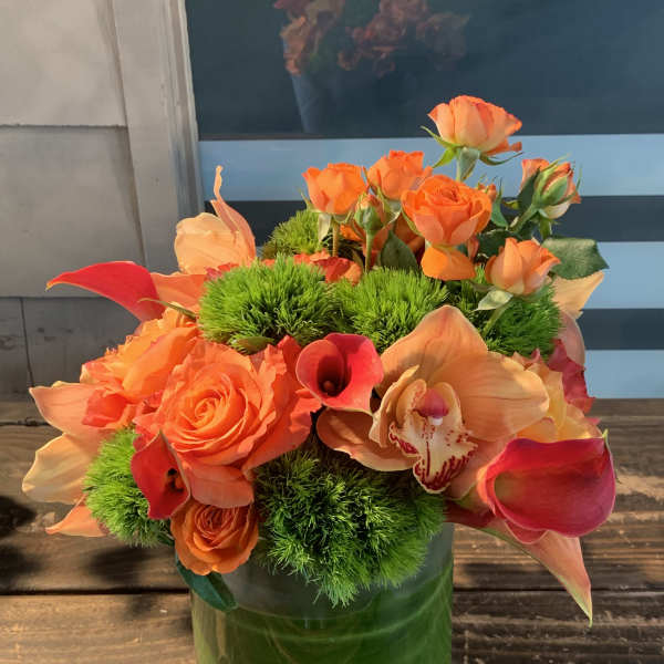 Orange roses and calla lilies in a green glass vase