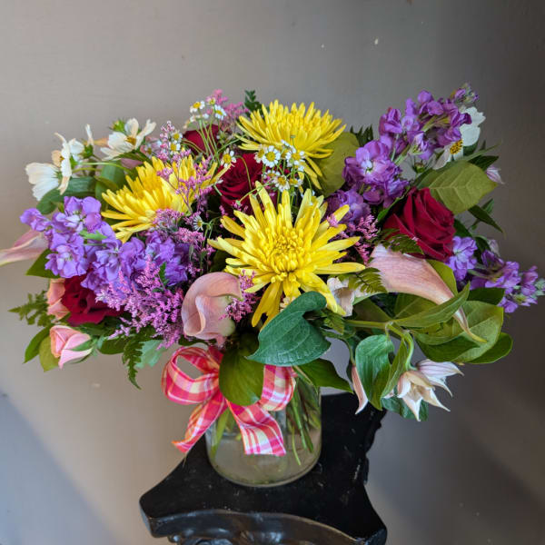 Mixed bouquet of yellow, purple, pink, and red flowers in a glass vase
