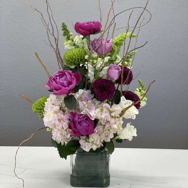 Pink and purple flowers arranged in a square glass vase with curly branches
