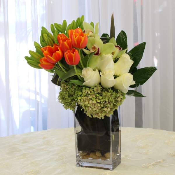Orange tulips and white roses in a tall glass vase