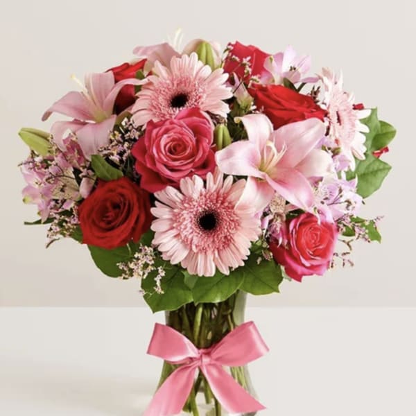 Bouquet of pink and red flowers in a clear glass vase with a pink ribbon