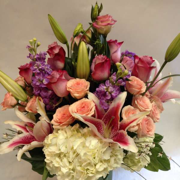 Mixed bouquet of pink roses, lilies, and white hydrangea in a glass vase