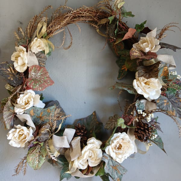 Floral wreath with cream roses and mixed foliage on a gray wall