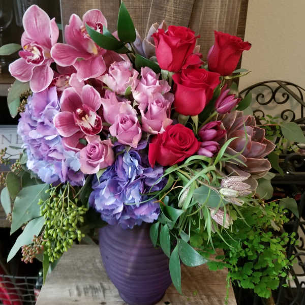 Bouquet of pink orchids, roses, hydrangeas, and succulents in a purple vase