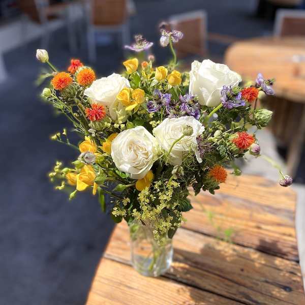 Mixed bouquet of white roses, yellow blooms, and orange flowers in a clear glass vase