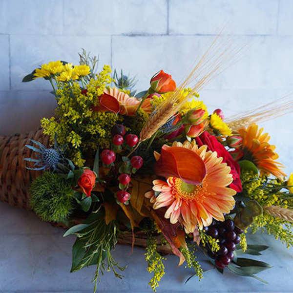 Cornucopia arrangement with orange and yellow flowers in a woven horn basket