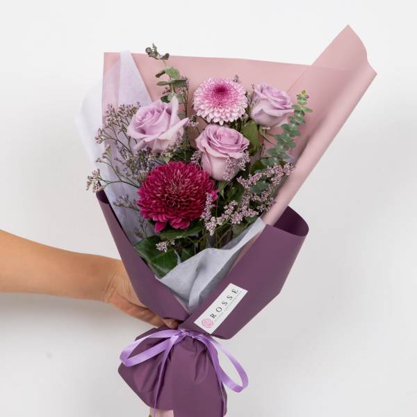 Handheld bouquet of pink roses and chrysanthemums wrapped in purple paper