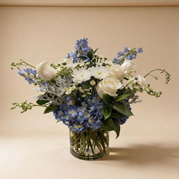 Blue and white arrangement with roses, mums, and hydrangeas in a clear glass cylinder vase