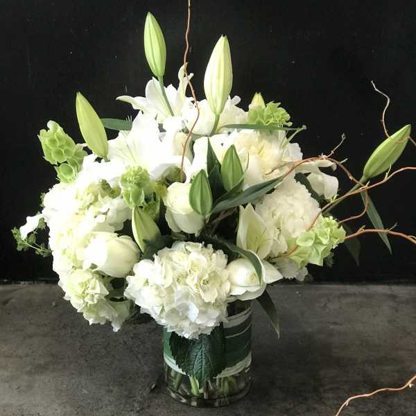 White lilies and hydrangeas in a glass vase with curly branches