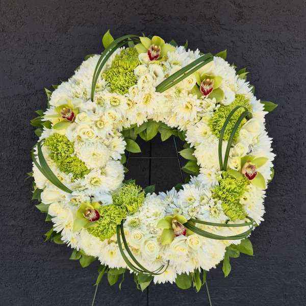 White and green floral wreath on a stand with orchids and chrysanthemums