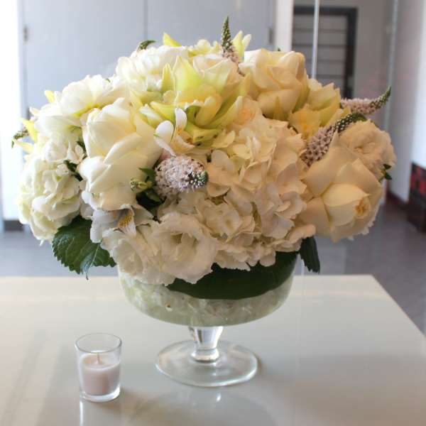 Cream and white floral arrangement in a glass pedestal vase