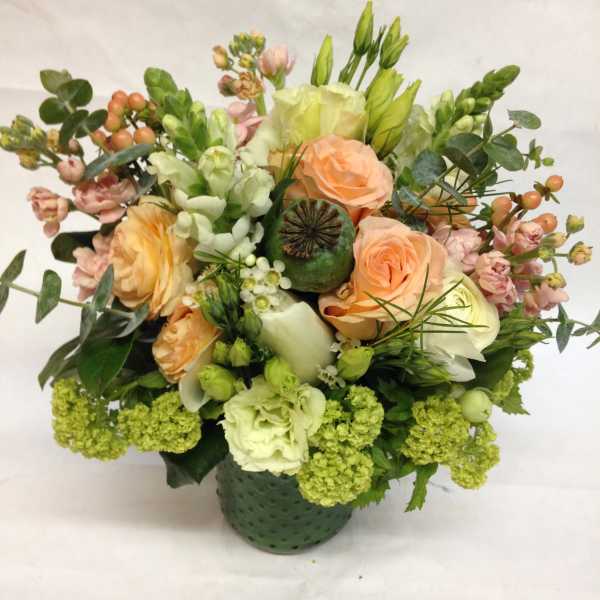 Mixed bouquet of peach roses, white blooms, and green flowers in a green vase