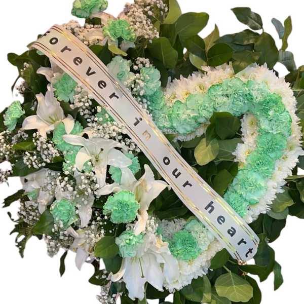 Heart-shaped floral wreath on an easel with a memorial ribbon