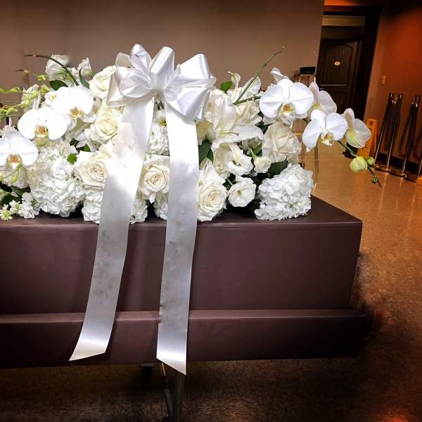 White floral casket spray with orchids, roses, and a large satin bow