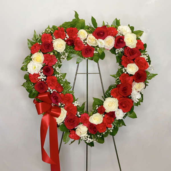 Heart-shaped wreath of red and white roses with a red ribbon on a stand