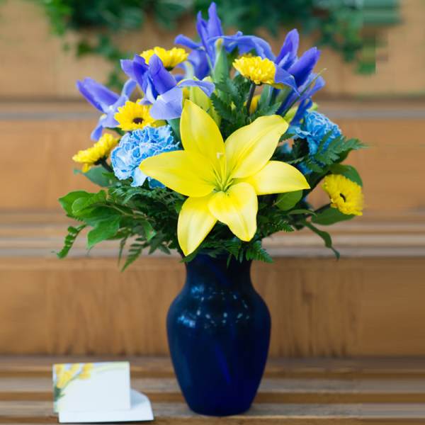 Blue vase holding yellow lilies and blue flowers