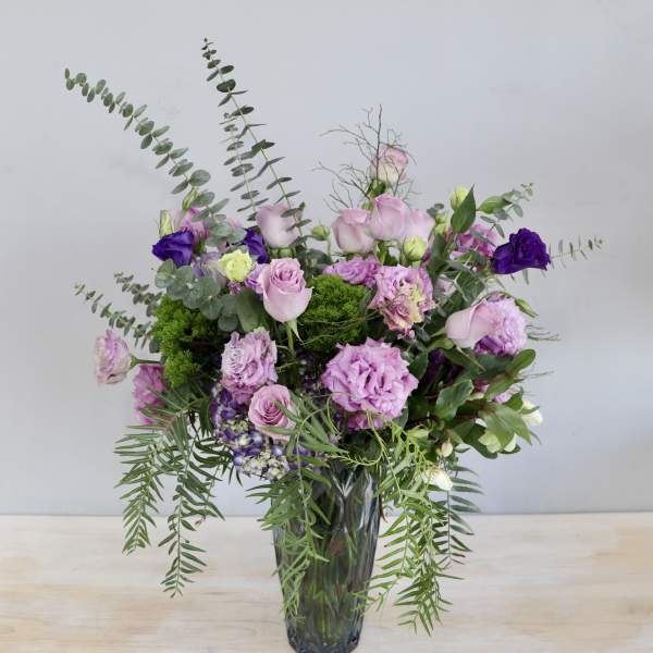 Pink and purple bouquet in a glass vase with trailing greenery