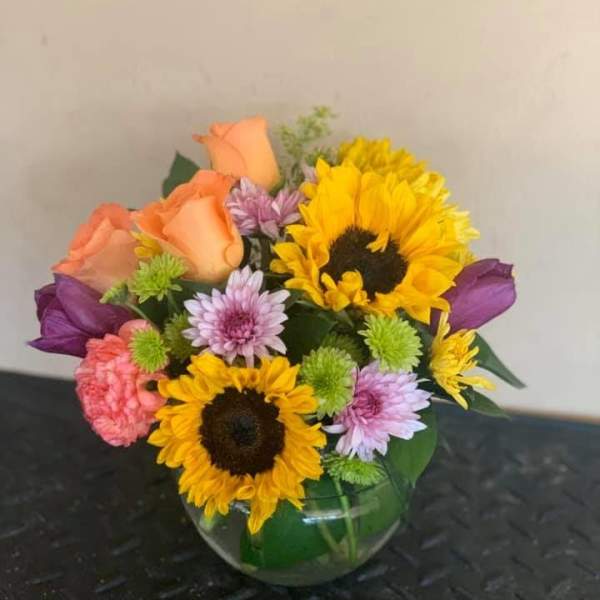 Mixed bouquet in a round glass vase with sunflowers, roses, and daisies
