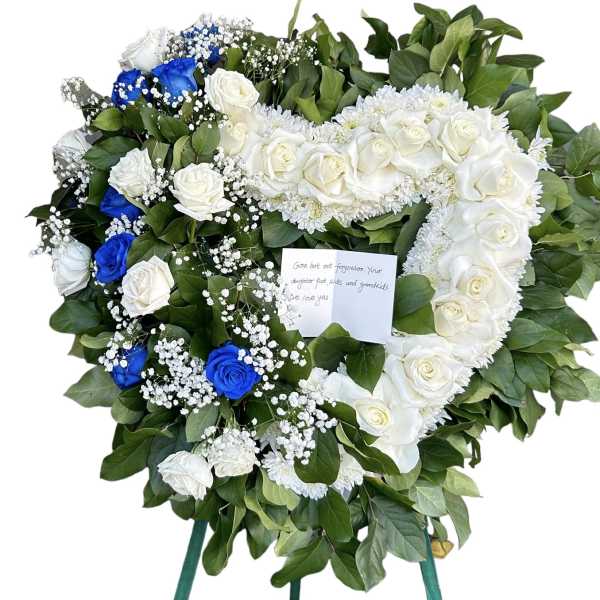 Heart-shaped funeral wreath of white and blue roses on a stand