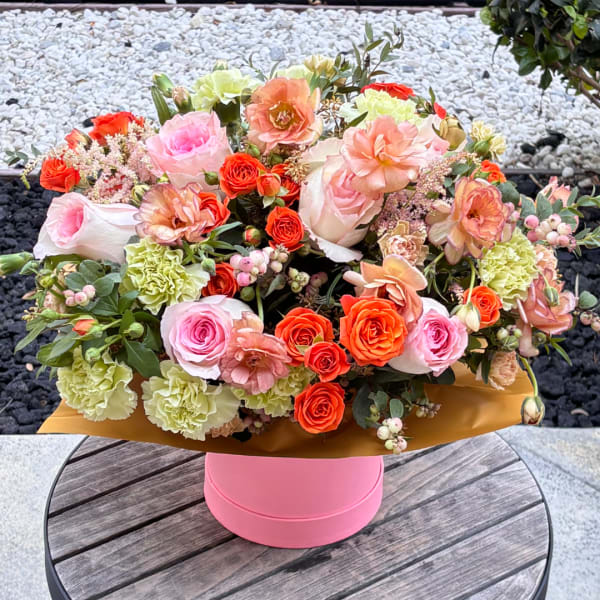 Mixed bouquet of pink, peach, and orange flowers in a pink box