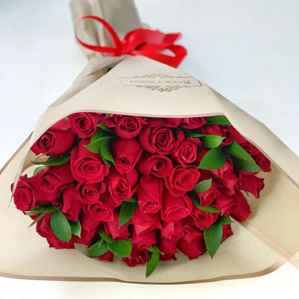 Large bouquet of red roses wrapped in cream paper and tied with a red ribbon